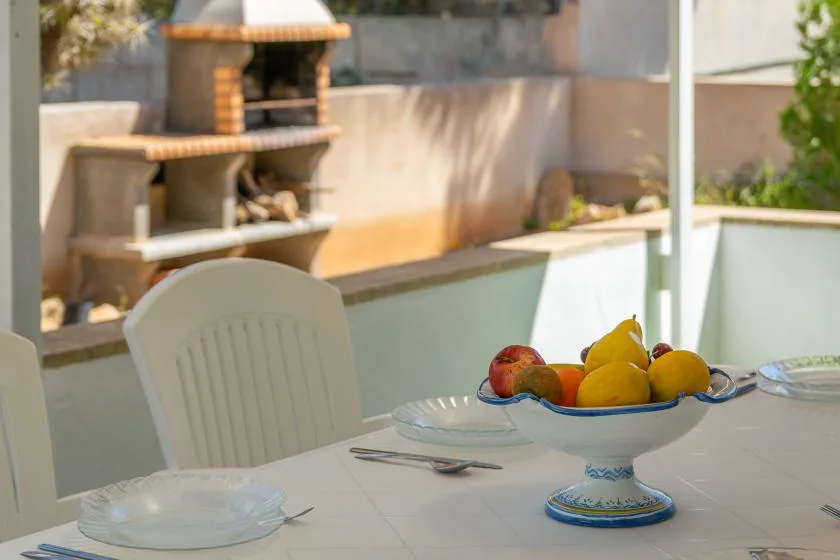 An outdoor dining table with a fruit bowl sits beside a built-in barbecue.