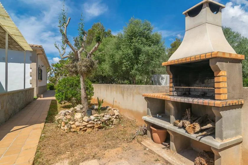 An outdoor patio with a built-in barbecue beside a paved walkway and garden.