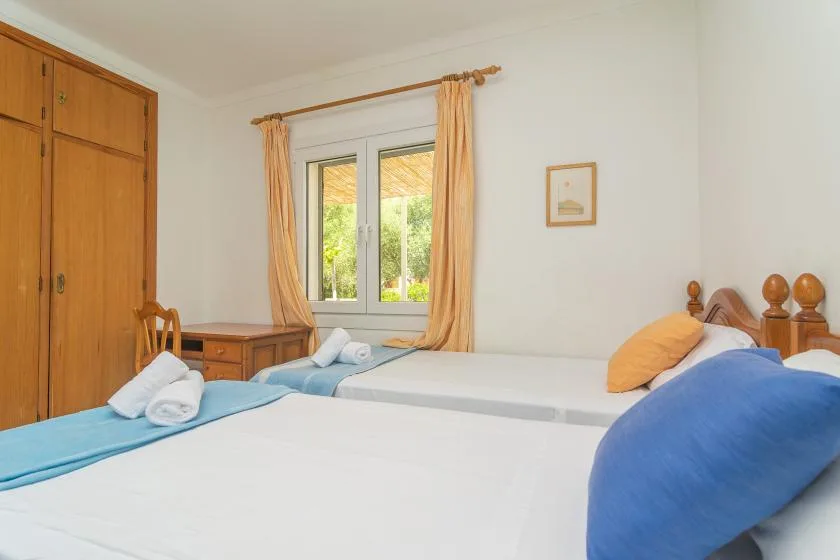 A bedroom with two beds, blue bedding, and a window with orange curtains.