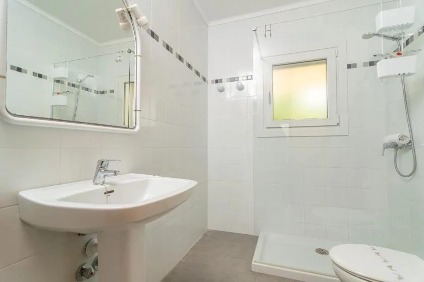 A bright tiled bathroom with a sink, shower, and small frosted window.