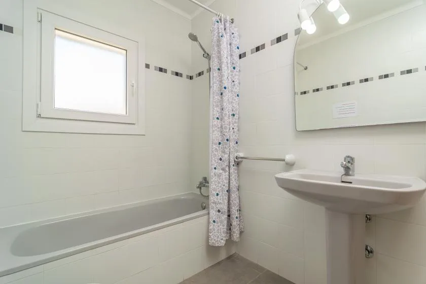 A bright bathroom with a bathtub, shower curtain, and sink.