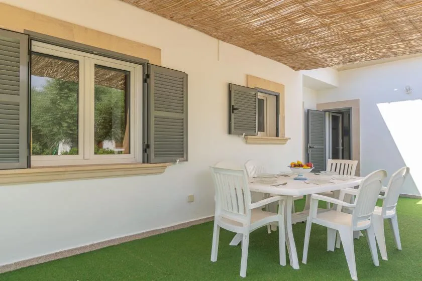 A covered outdoor dining area with a table and white seating.