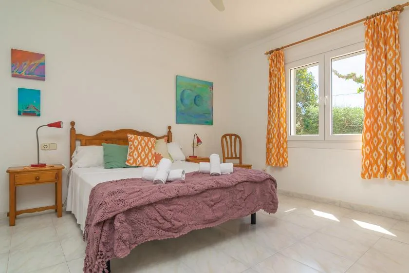 A bright bedroom with a double bed and orange curtains beside the window.