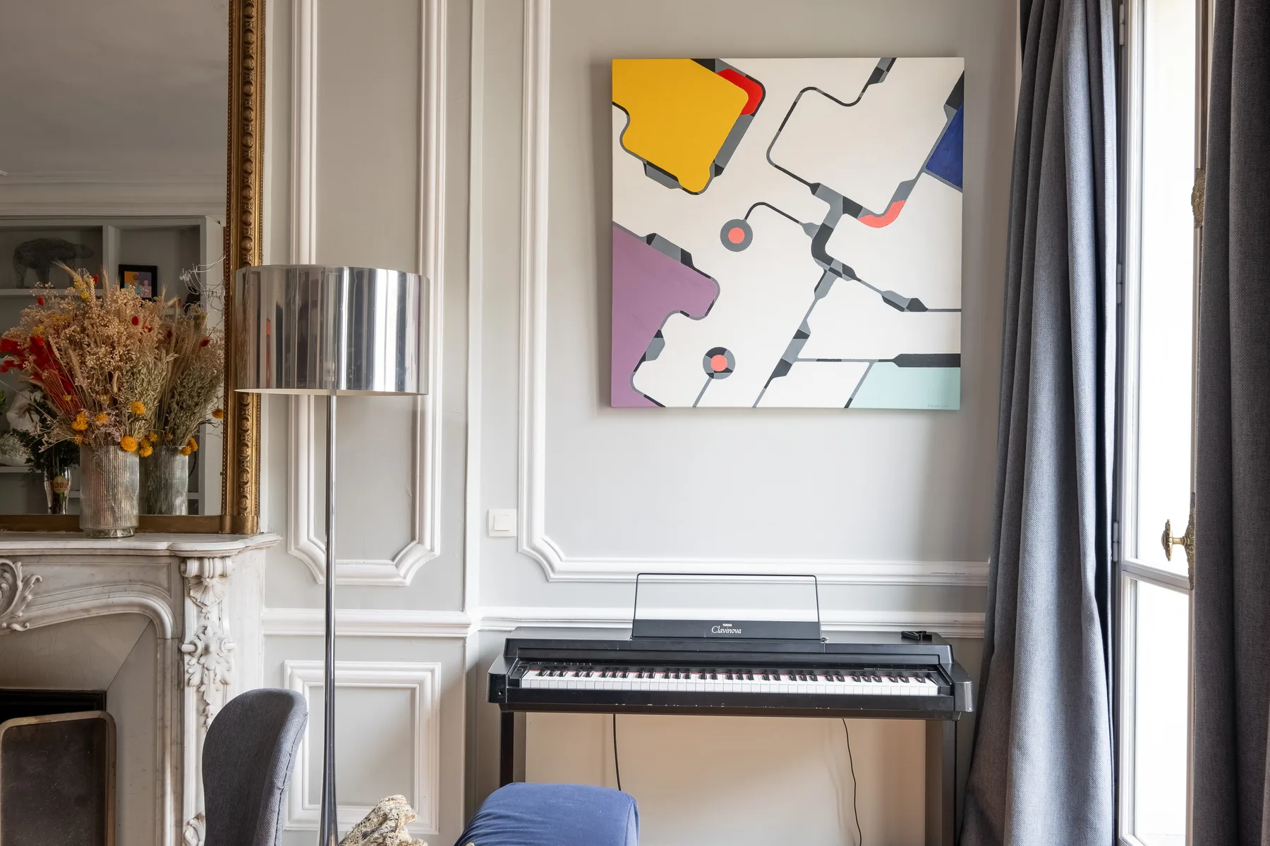 Un teclado está bajo una obra abstracta colorida en una habitación luminosa con paneles.