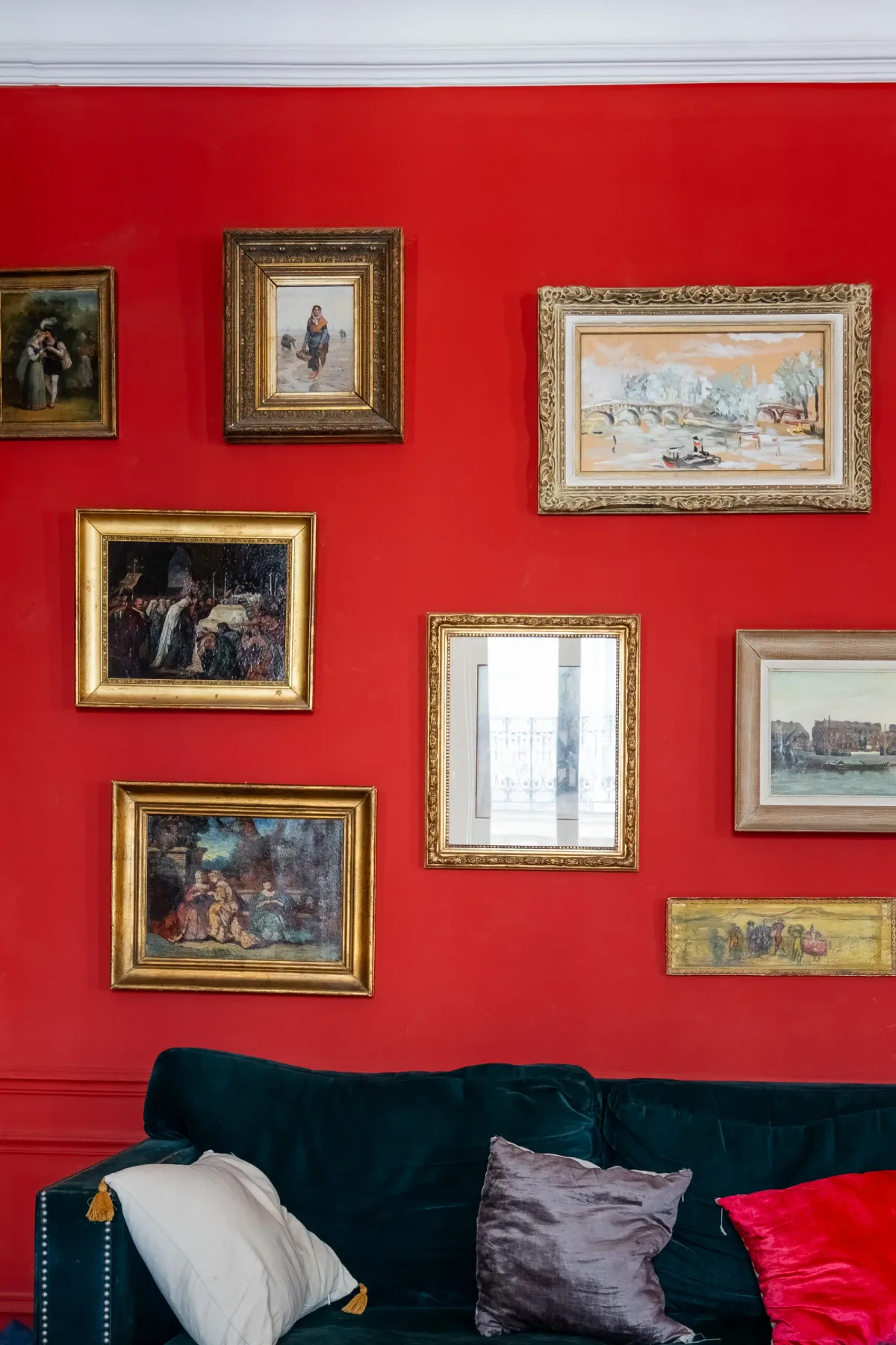 Una sala de estar con un sofá oscuro frente a una pared roja decorada con cuadros enmarcados.