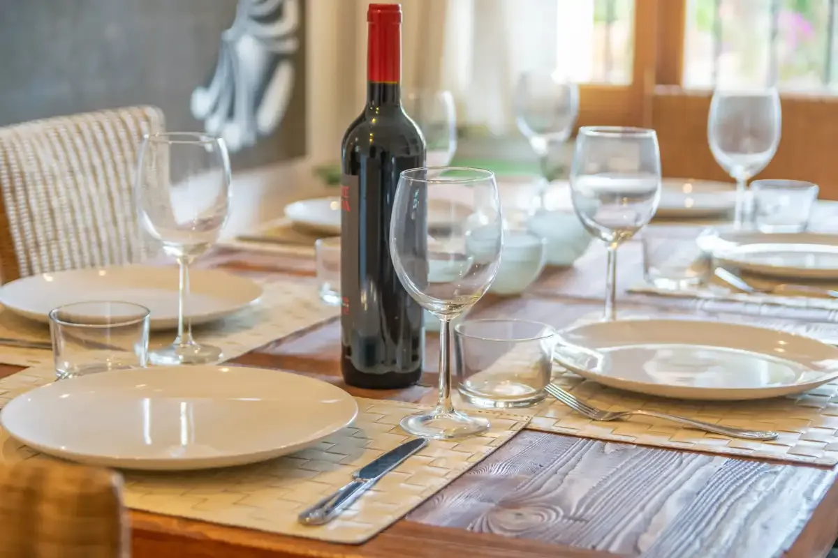 A dining table set with plates, glasses, and a bottle of wine.