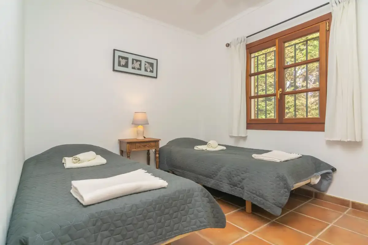 A bedroom with two beds, folded towels, and a wooden-framed window.