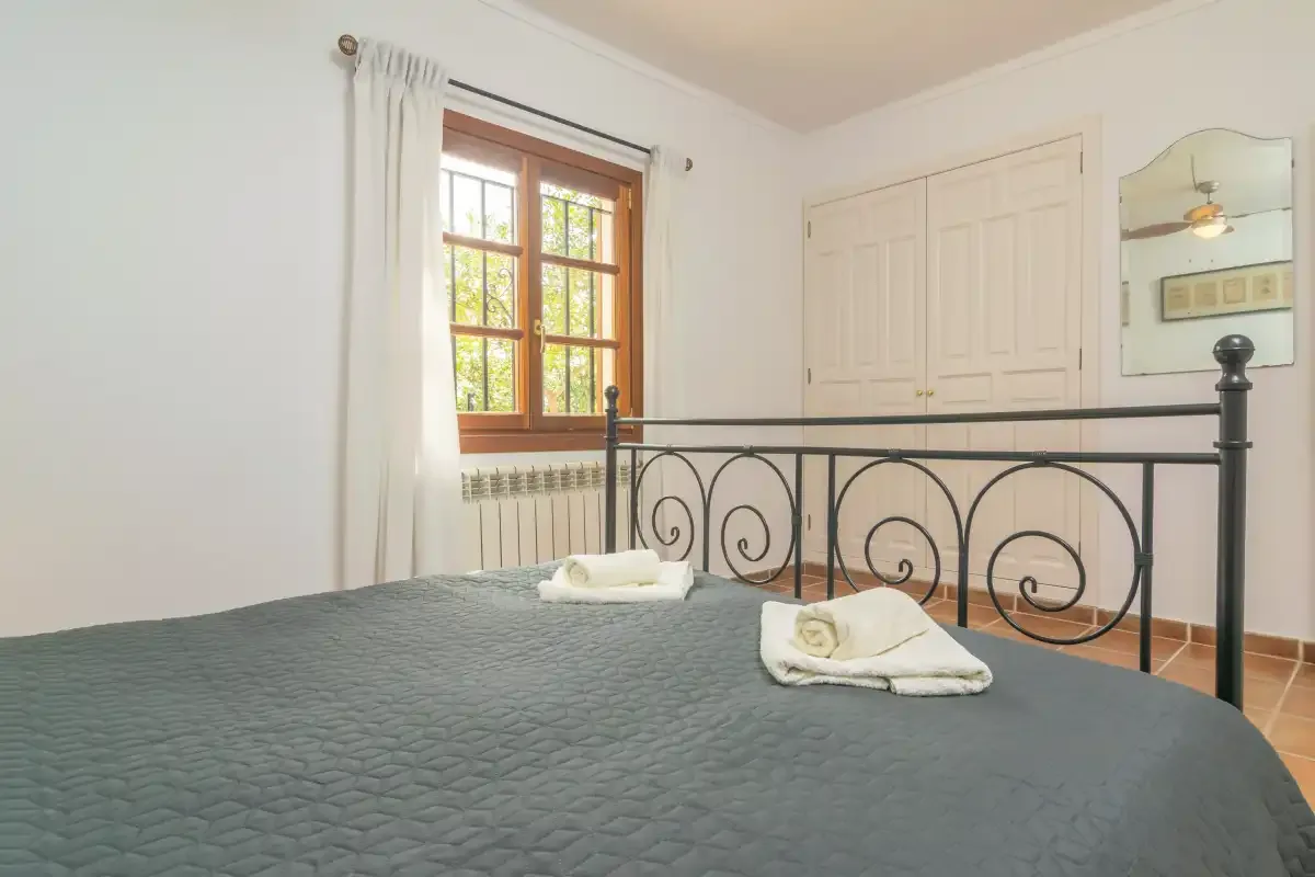 A bedroom with a dark bedspread, folded towels, and a window with curtains.