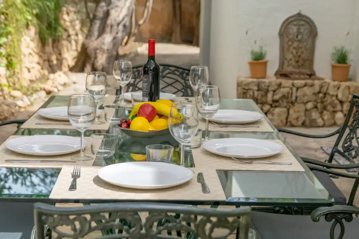 A set dining table sits outdoors beside a stone wall and potted plants.