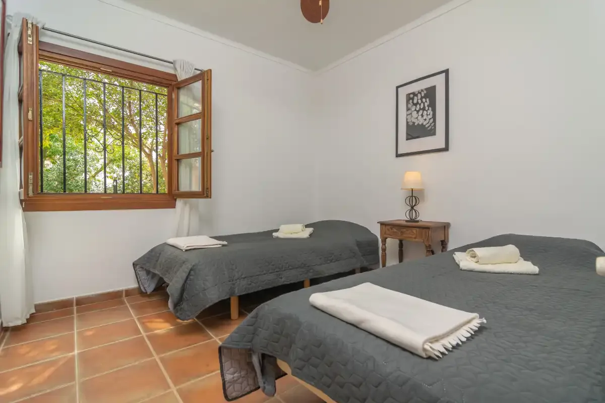 A bedroom with two beds, a wooden bedside table, and an open window.