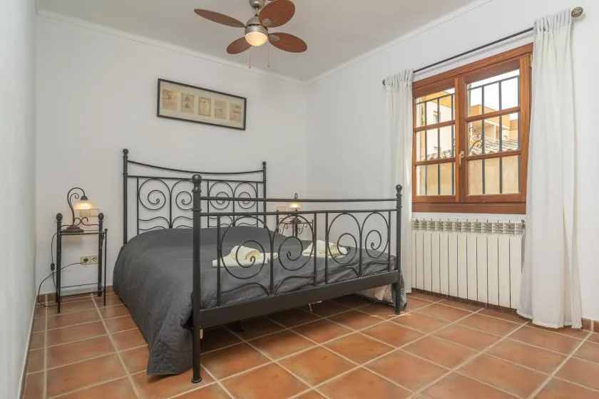 A bedroom with a black metal bed, a window, and tiled flooring.