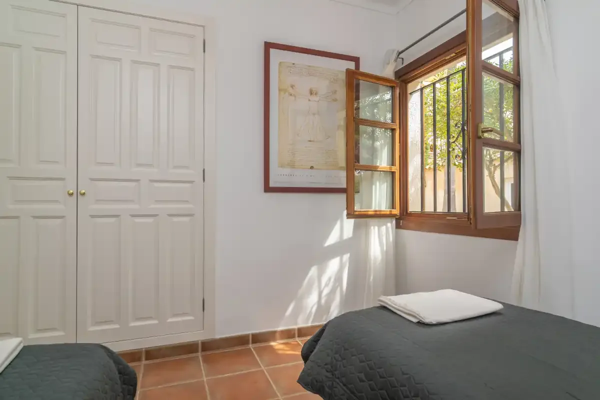 A bedroom with beds beside an open wooden-framed window.