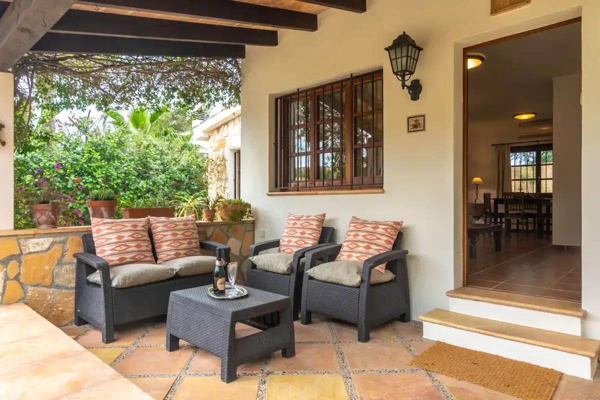 A covered patio has cushioned seating and a view of the garden.