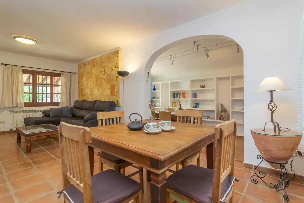 A dining area with a wooden table and chairs opens onto a living room.