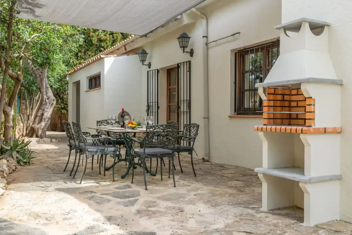 A shaded outdoor dining area with a table and built-in barbecue.