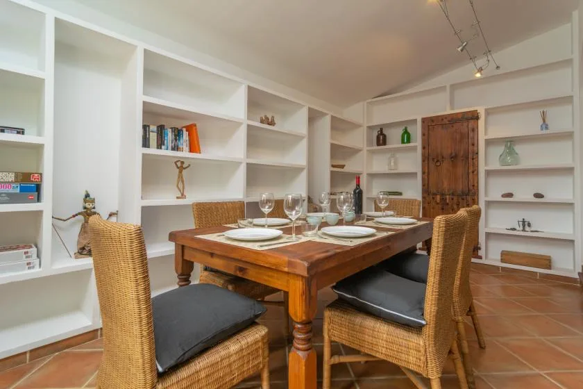 A dining area with a wooden table, wicker seating, and built-in white shelves.