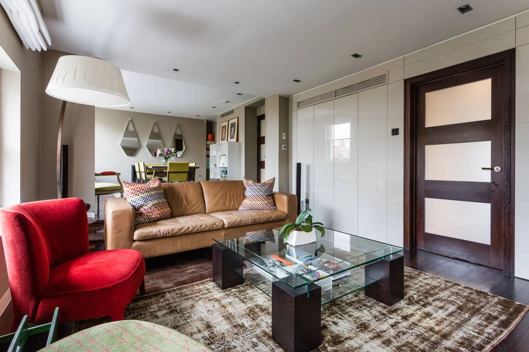 Una sala de estar con un sofá beige, un sillón rojo y una mesa de centro de vidrio.