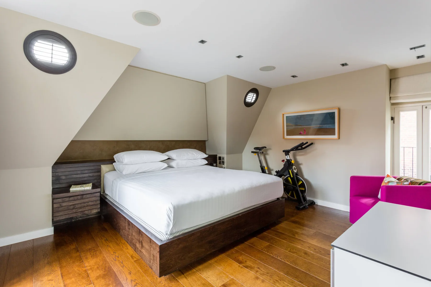 A bedroom with a large bed, exercise bikes, and a bright pink chair.