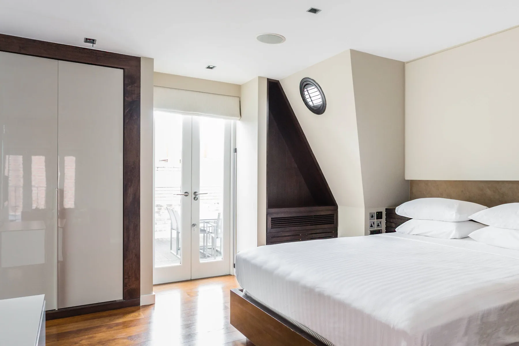 A bedroom with a large bed beside a glass door and a dark triangular fireplace.