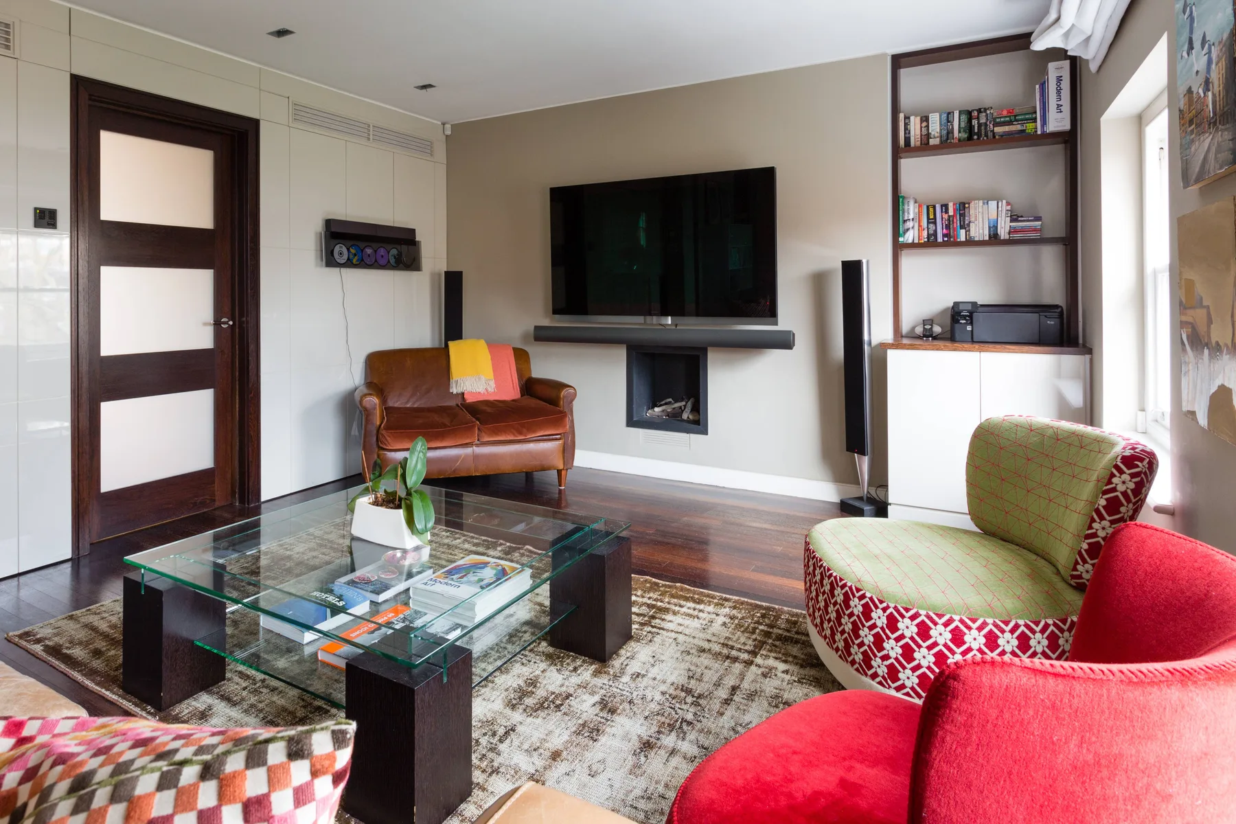 Una sala de estar con un televisor sobre una chimenea y asientos alrededor de una mesa de centro de vidrio.