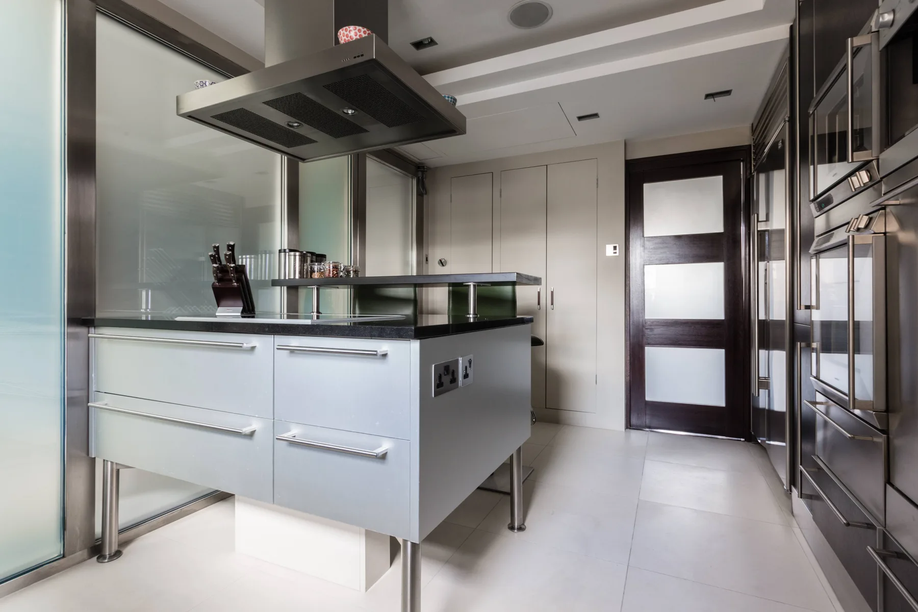 A modern kitchen with a central island, stainless steel appliances, and a dark-framed door.