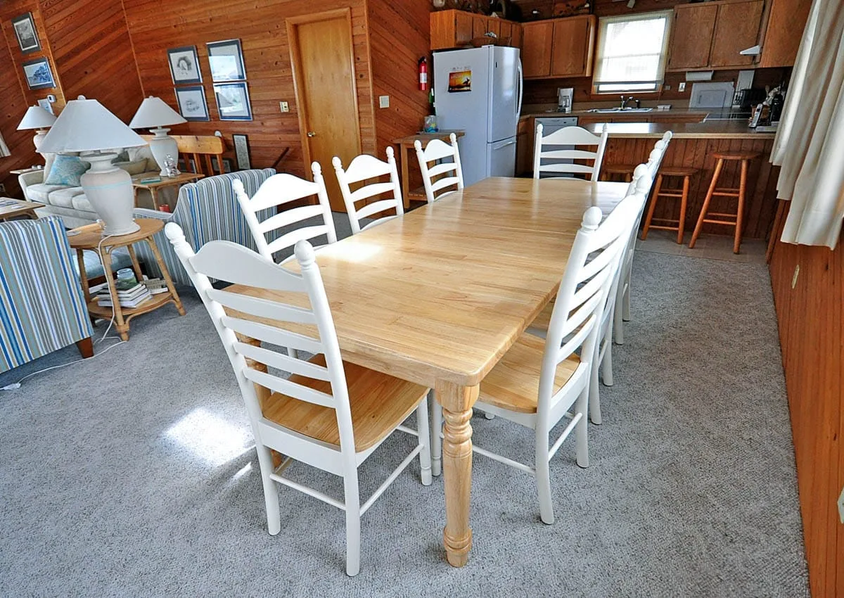 Comedor con una mesa de madera y sillas blancas junto a la cocina.