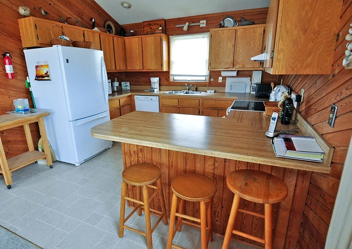 Cocina revestida de madera con una isla central y taburetes.