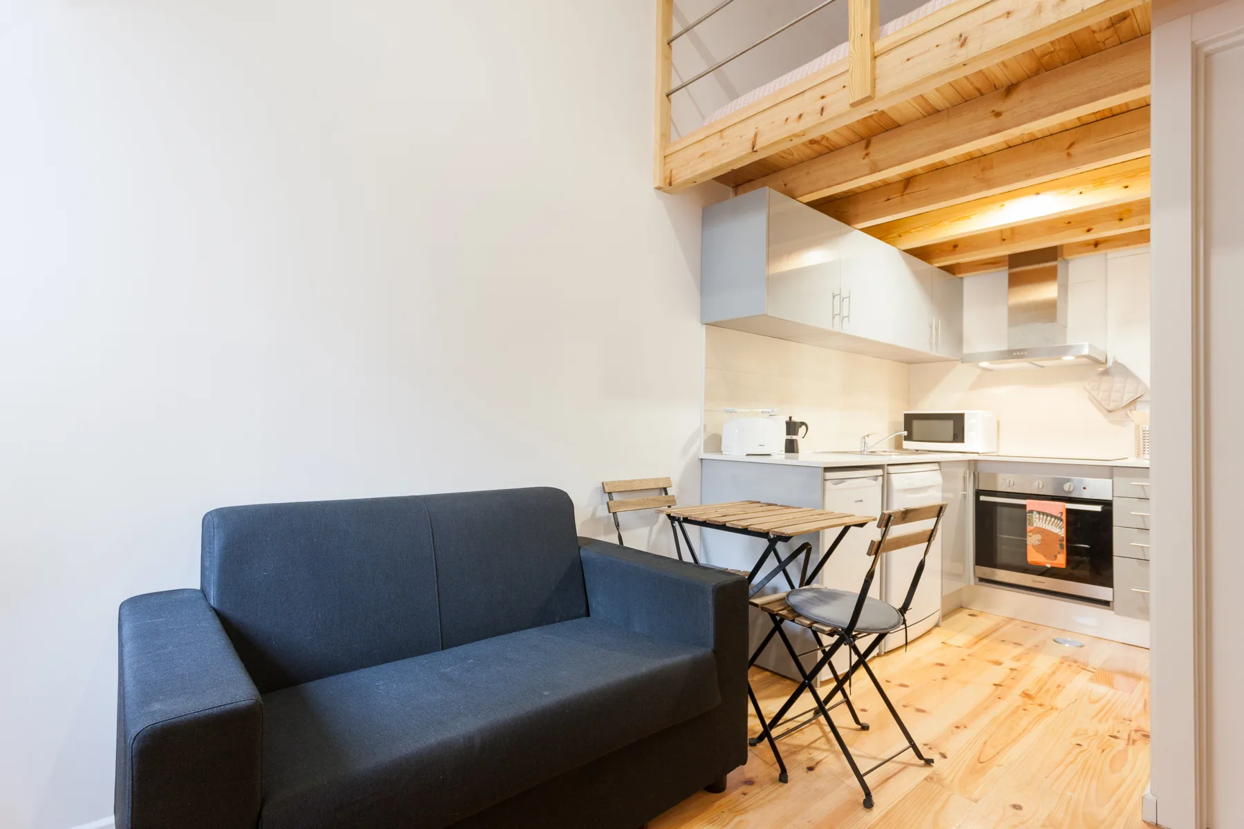 A compact studio living area with a dark sofa, dining table, and kitchenette.