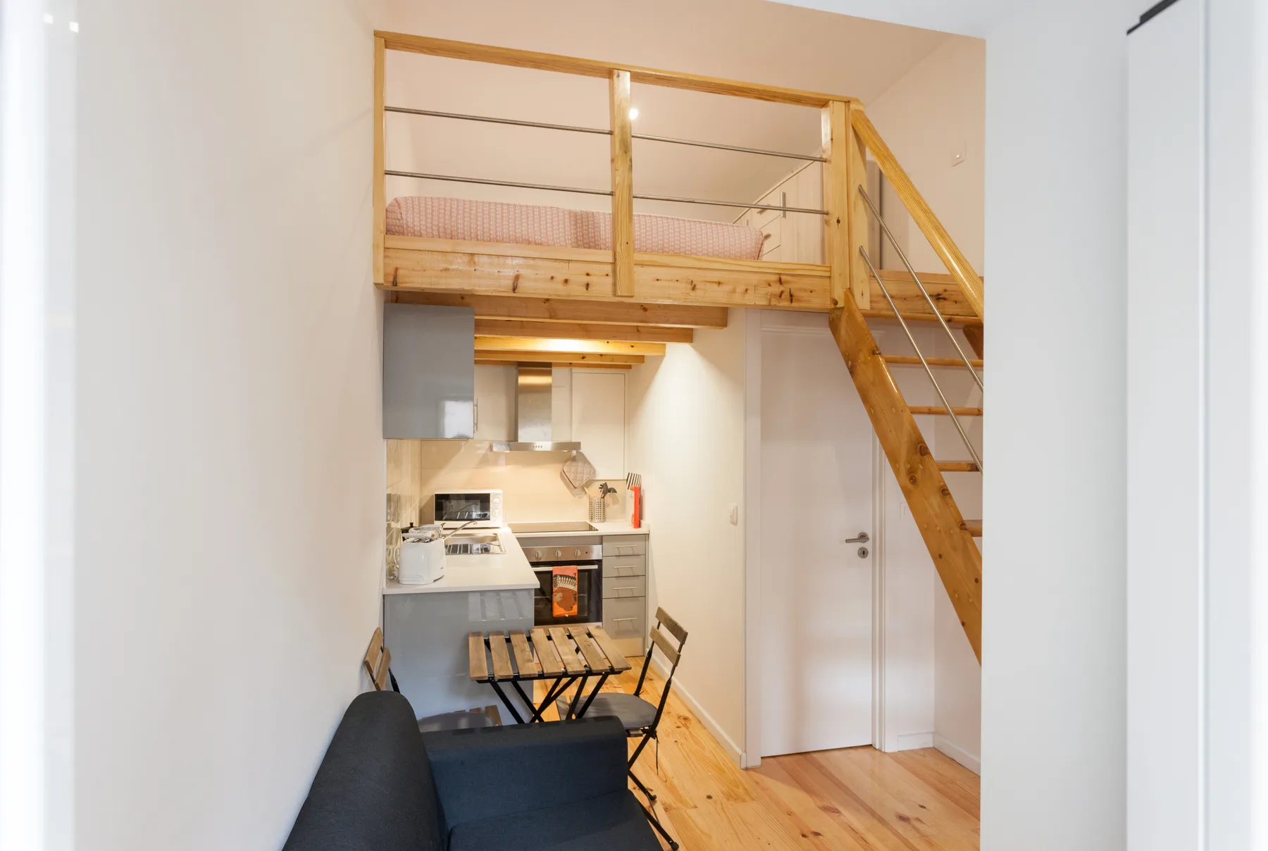 Un estudio compacto con cocina, mesa de comedor y zona elevada para dormir.