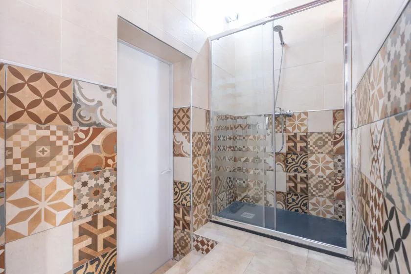 A tiled bathroom with a glass shower and patterned wall tiles.