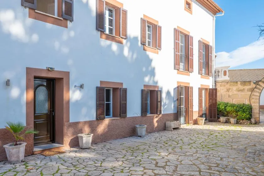 A white building exterior with brown shutters and a stone-paved courtyard.