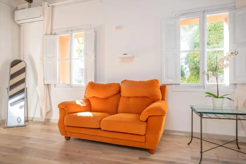 A living room with an orange sofa beneath open windows.