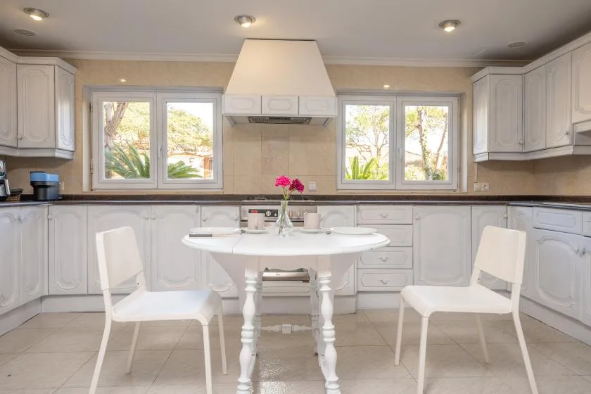 A bright kitchen with white cabinetry, a central table, and windows.