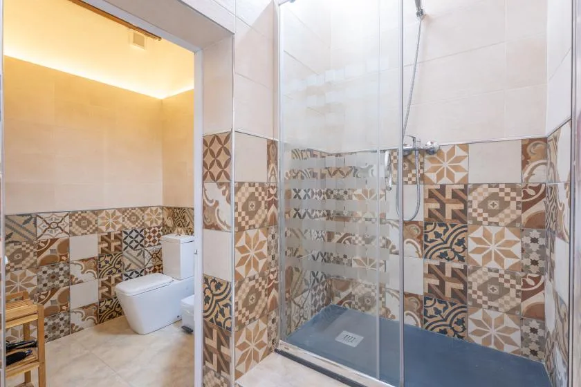 A bathroom with a glass shower and patterned tile walls.