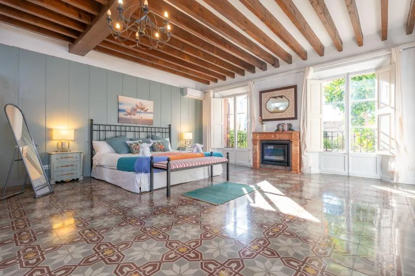 A bright bedroom with a bed, fireplace, and patterned tile floor.