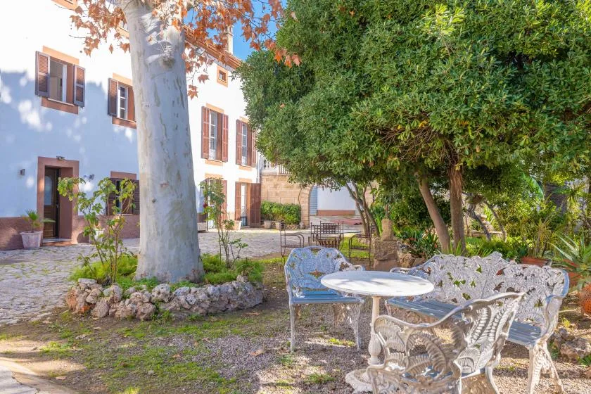A shaded garden seating area beside a white building, with trees and outdoor tables.