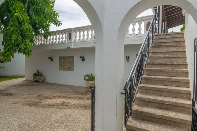 A white courtyard with arched openings, an upper balcony, and stairs.