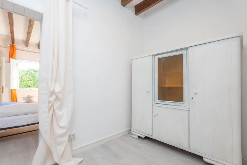A bright bedroom with a bed partly visible beside a white wardrobe.
