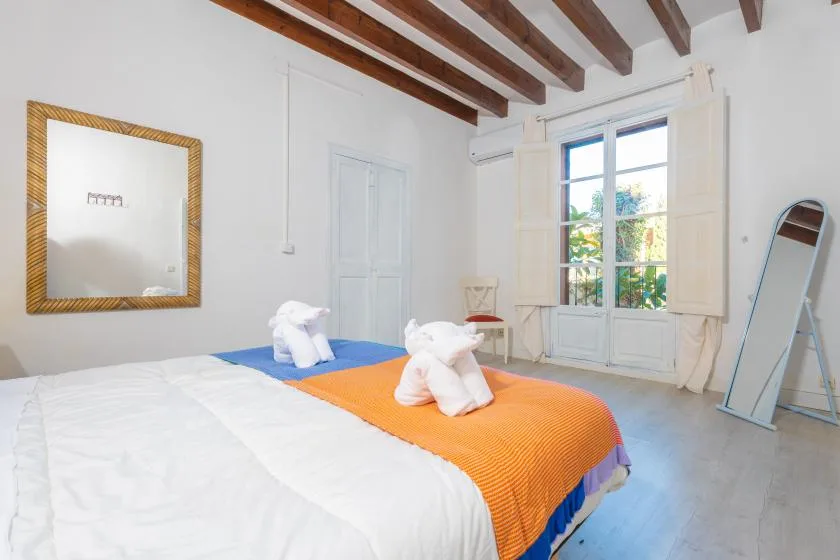 A bright bedroom with two beds, exposed ceiling beams, and a large window.