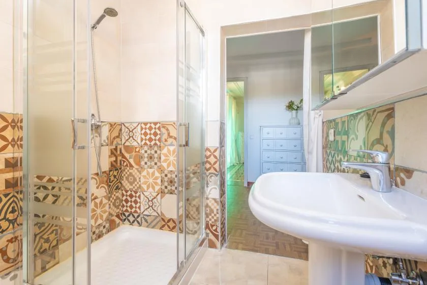 A bathroom with a glass shower, patterned wall tiles, and a sink.