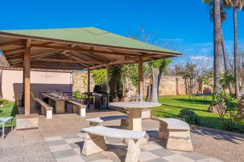 A covered outdoor dining area with stone tables and a grill overlooks a garden.
