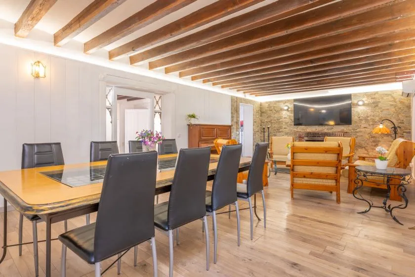 Dining and living area with a long table, seating, and a wall-mounted television.