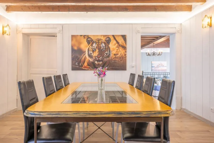 Dining room with a long table, seating, and a tiger painting on the wall.