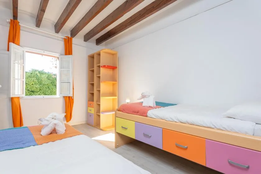 A bright bedroom with two beds, colorful storage drawers, and an open window.