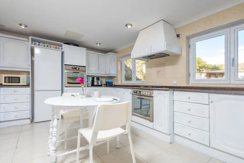 A bright kitchen with white cabinets, a dining table, and large windows.
