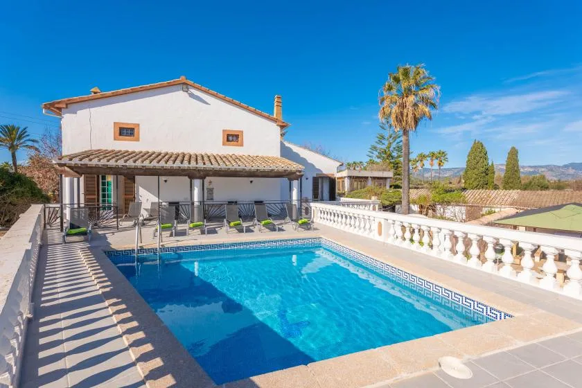 Outdoor swimming pool beside a white house with a shaded patio.
