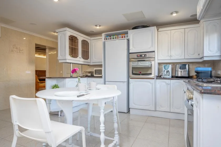 A bright kitchen with white cabinetry, appliances, and a round dining table.
