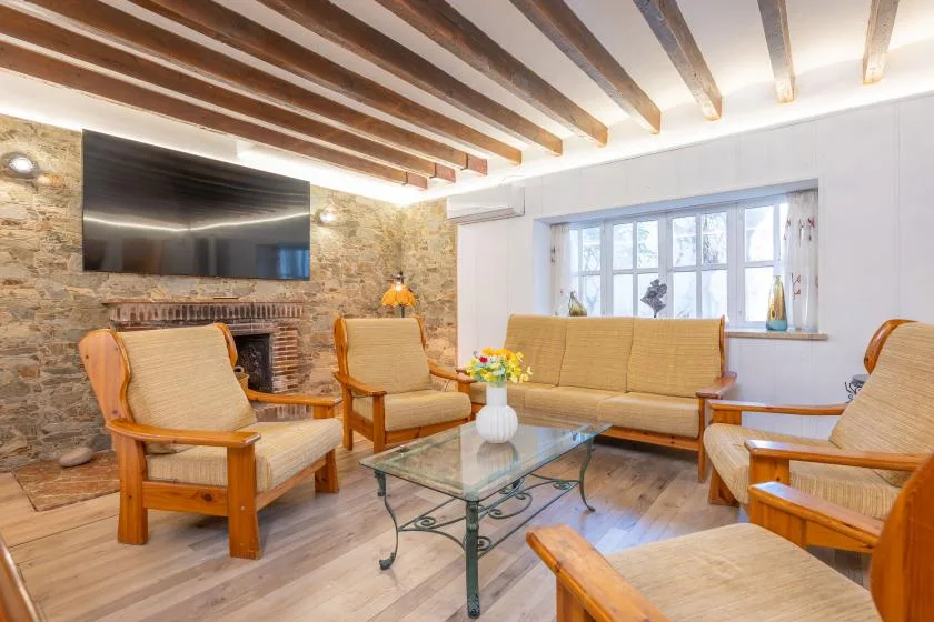 A living room with wooden seating, a glass coffee table, and exposed ceiling beams.