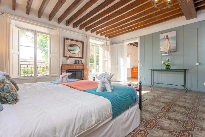 A bedroom with a large bed, tall windows, and exposed wooden ceiling beams.