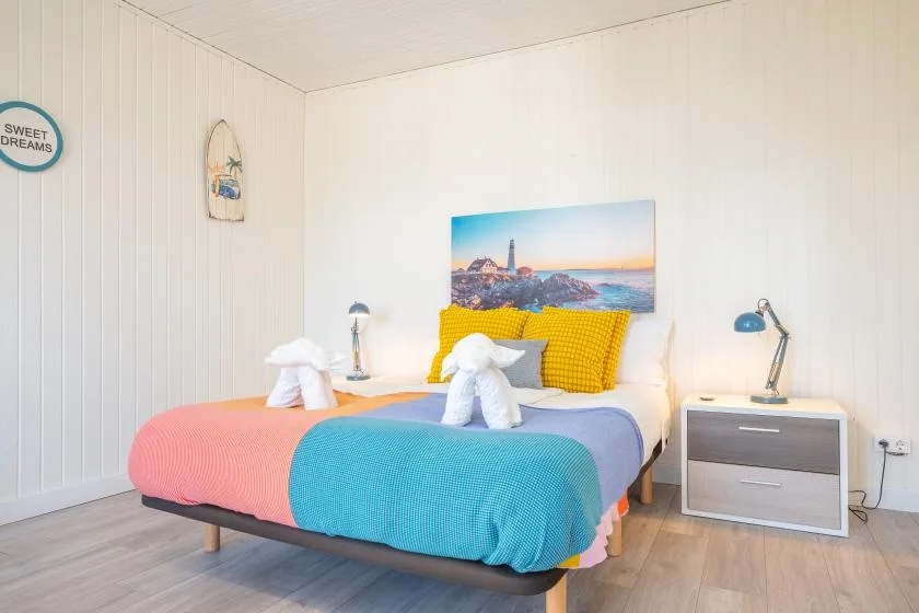 A bright bedroom with a colorful bed and a coastal picture above it.